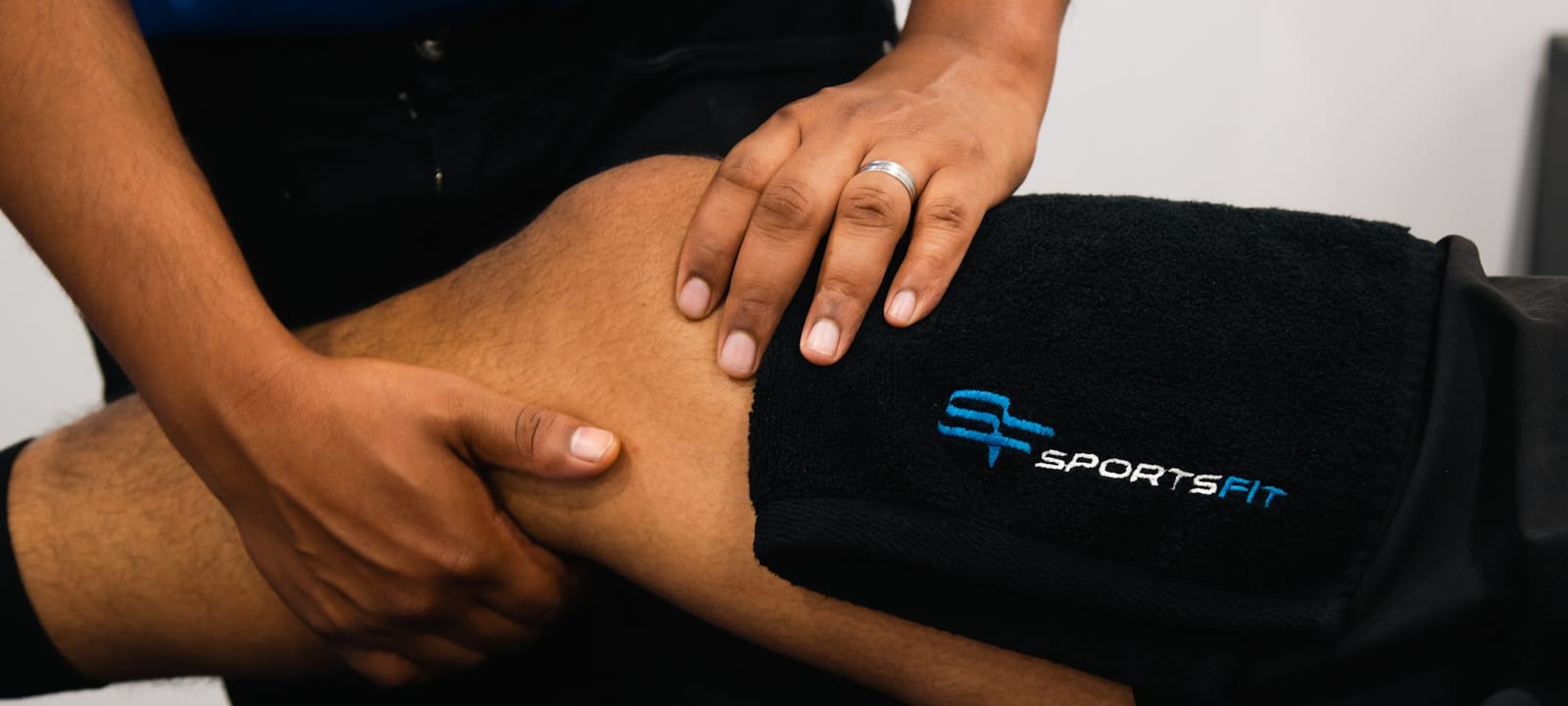 A physio’s hands assessing a knee over a SportsFit towel