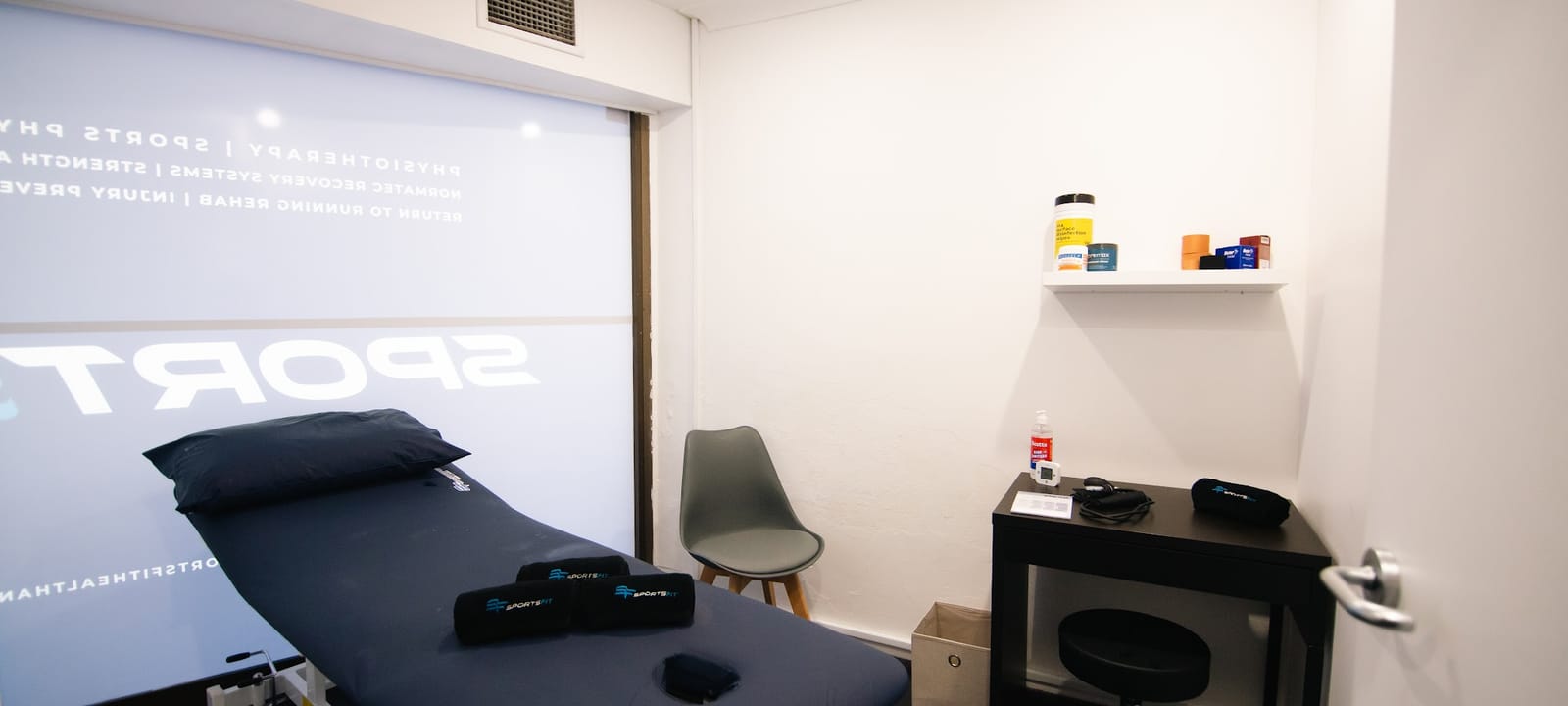 An empty treatment room at SportsFit Five Dock: plinth, chair and supply shelf